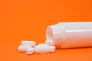 Large white pills spill out of a white jar on an orange background