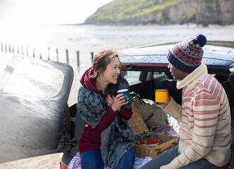 Happy couple drinking coffee at back of car on beach
