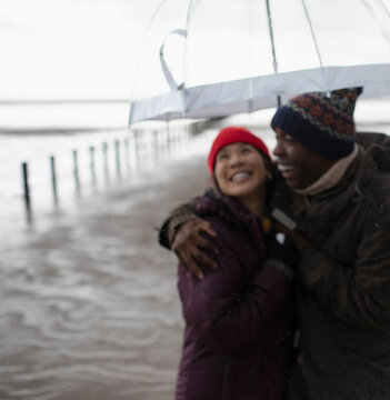 Happy couple in warm clothing under umbrella on wet winter beach