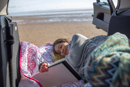 Serene woman with sketchbook at back of car on beach