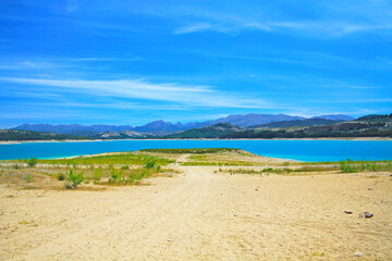 Beautiful idyllic calm blue turquoise mountain swimming lake, empty sand beach, blue summer sky - Reservoir Vinuela, Malaga area, Spain