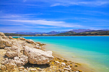 Fototapeta na wymiar Beautiful calm blue turquoise mountain swimming lake, empty sand beach - Reservoir Vinuela, Malaga area