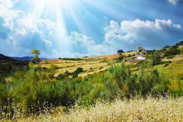 Typical andalusian calm mountain valley landscape, sun rays, low morning clouds, idyllic white farm house in rock front, agricultural fields - Spain, Andalusia