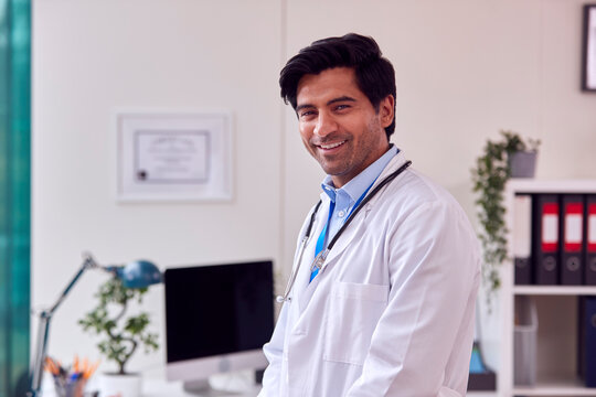 Portrait Of Male Doctor Or GP with Stethoscope Wearing White Coat Standing In Office