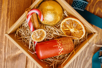 Top view of christmas gift box and decorations on wooden table. New Year's atmosphere. Candy cane, candle with ornate, ribbon, dried orange, golden ball, cinnamon. Festive still life.