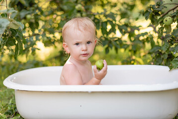 beautiful child bathes in white bath  eats green apple