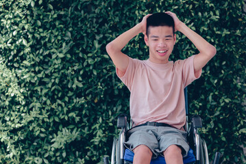 Young man with disability with happy face by with cheerfulness in nature green background, Teenager boy sitting with tray for activities on wheelchair, Good mental health and positive picture concept.