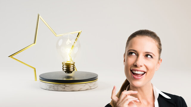 businesswoman and a lightbulb on a stage with a golden star in front of light grey background