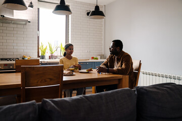 Black man smiling while having lunch with his daughter at home