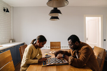 Black girl and her father playing checkers at home