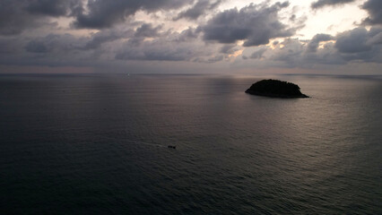 Fototapeta na wymiar Beautiful sunset with clouds, sea and island. A small Thai ship is sailing. Clouds are reflected on the water. A lonely island stands in the distance. Top view from a drone. Calm ocean at sunset