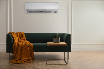 Modern air conditioner on white wall in room with stylish green sofa