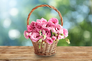 Beautiful pink Eustoma flowers in wicker basket on wooden table outdoors. Bokeh effect