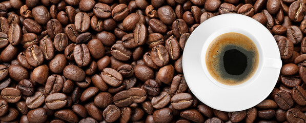 Cup of tasty aromatic coffee on roasted beans, top view. Banner design