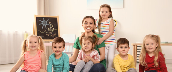 Kindergarten teacher with group of children in playroom. Banner design