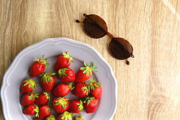 Lilac plate with fresh strawberries and round retro sunglasses on the table. Flat lay. 
