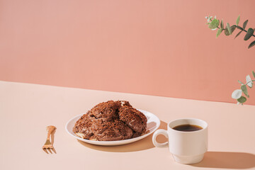 Cake on plate with golden fork and cup of coffee on the table against pink background.