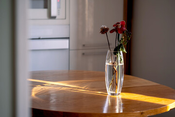 A bouquet in a transparent vase on a wooden table in the rays of the sun.