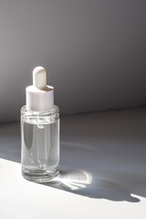 A white transparent bottle with serum in the rays of the sun.