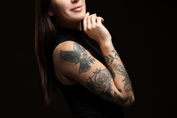 Woman with tattoos on arm against black background, closeup