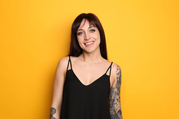 Beautiful woman with tattoos on arms against yellow background