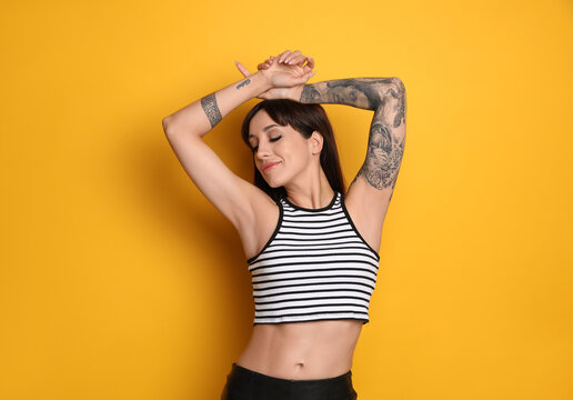 Beautiful woman with tattoos on arms against yellow background