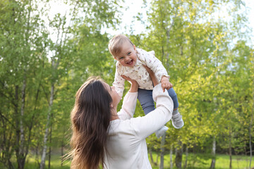 Happy mother playing with her cute baby in park on sunny day