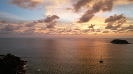 Luxury yacht at an epic sunset with a view of the island and incredible orange clouds. The sky is reflected in the water. A lonely island in the distance. Calm. Top view from drone. Kata Beach Phuket
