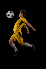 Naklejka premium Dynamic portrait of professional football, soccer player training with ball isolated on dark background. Concept of sport, match, active lifestyle, goal and hobby