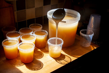 Apiculteur remplissant avec une louche des pots de miel posés sur une  table à coté du seau...