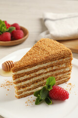 Slice of delicious layered honey cake with mint and raspberry on plate, closeup