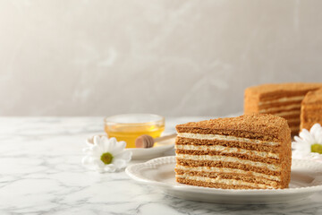 Fototapeta na wymiar Slice of delicious layered honey cake served on white marble table. Space for text