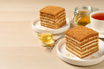 Fototapeta na wymiar Delicious layered honey cake served with tea on wooden table. Space for text
