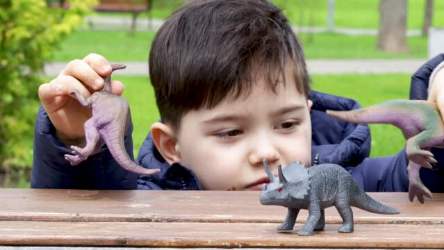 cute kid is playing with  dinosaurs toys on park bench, spring, green nature, grass. happy dinosaur day, may 15 and june 1. fascinating dinosaur fantasies. spring outside, public park,having fun.