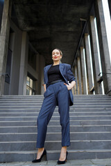 Business woman with hands in pocket posing against the backdrop of a modern building