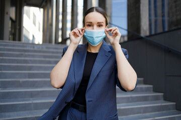 Fototapeta premium Portrait of elegant business woman in a blue suit putting on a medical mask during epidemic