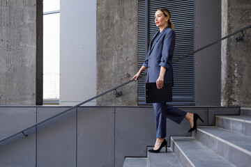 Pretty business woman walking down the stairs with a folder for documents in her hand