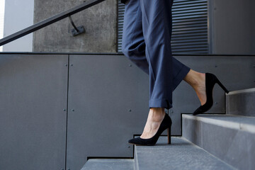 Close-up of a business woman's legs in pants and high-heeled shoes walking down the stairs - obrazy, fototapety, plakaty
