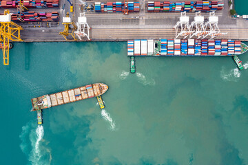 Aerial top view Tugboat pushing container ship to commercial port load and unloading of goods container import export international in green sea