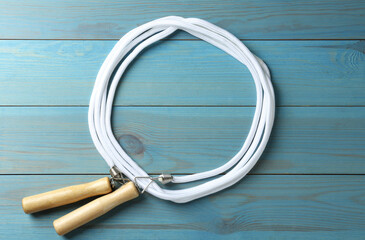 Skipping rope on light blue wooden table, top view. Sports equipment