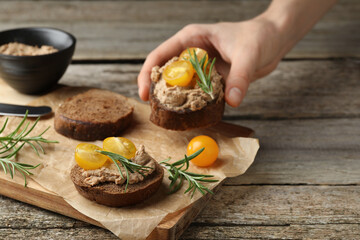 Woman taking slice of bread with delicious pate and tomatoes from board at wooden table, closeup