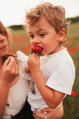 Mother and son hugging and eating strawberries in a poppy field.
