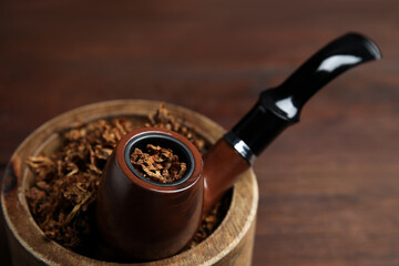 Smoking pipe and bowl of dry tobacco on table, closeup