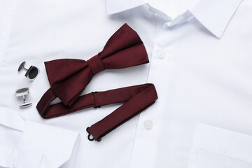 Stylish burgundy bow tie and cufflinks on white shirt, top view
