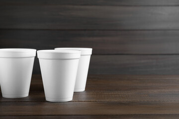 White styrofoam cups on wooden table, space for text