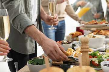 Man with glass of champagne taking food from buffet indoors, closeup. Brunch table setting