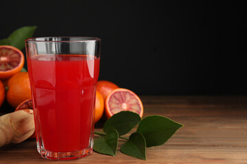 Tasty sicilian orange juice in glass, fruits and squeezer on wooden table, space for text