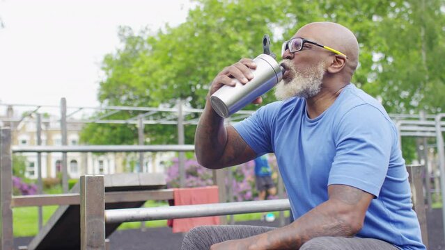 Senior black male recovering after training with a bottled drink, in slow motion