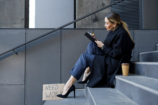 Unemployed Business Woman Sits On The Stairs Near The Building And Fills Resume