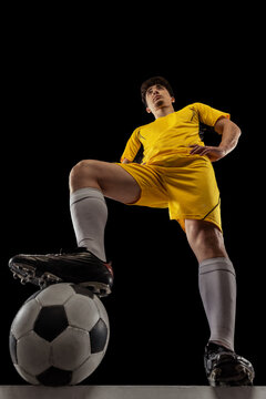 Bottom view of young professional football, soccer player standing with ball isolated on dark background. Concept of sport, match, active lifestyle, goal and hobby